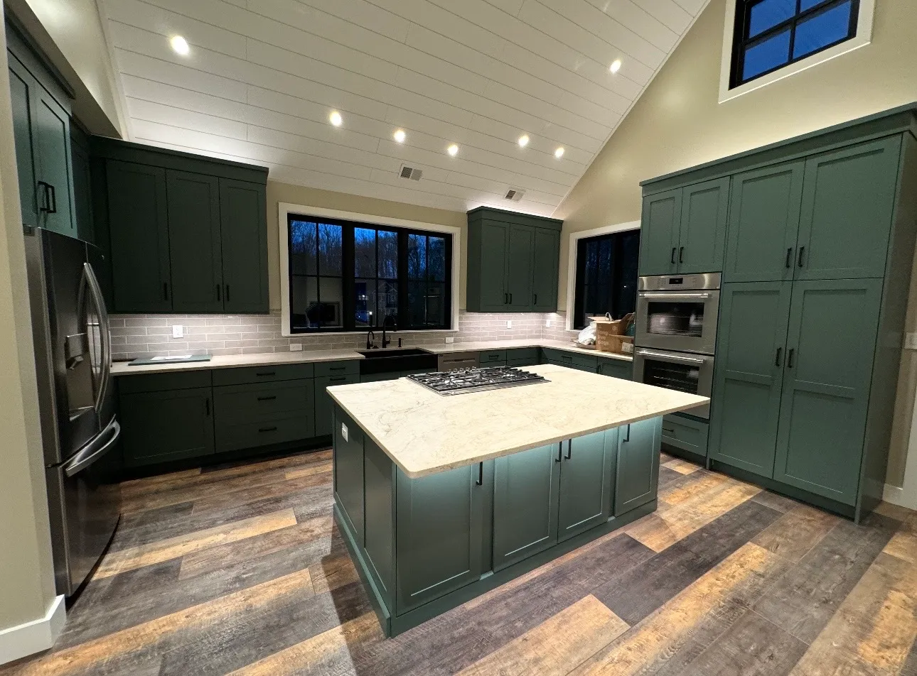Kitchen with dark green shaker cabinets, a marble-topped island with a gas cooktop, a vaulted white shiplap ceiling and wide-plank wood floors